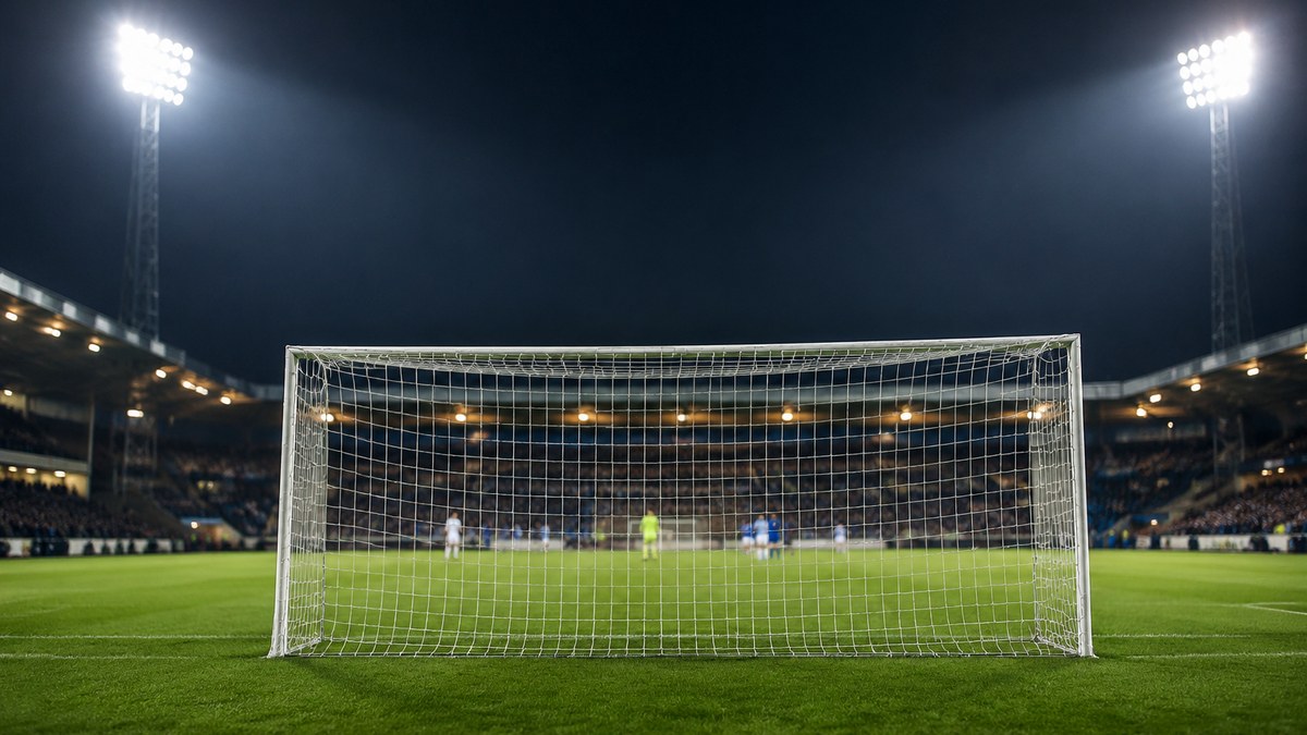 Campo de fútbol iluminado de noche en Dinamarca, con la portería y las gradas al fondo.