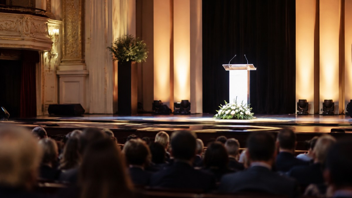 Escenario de una ceremonia de premios en Madrid, con un atril y asistentes vistos de espaldas.