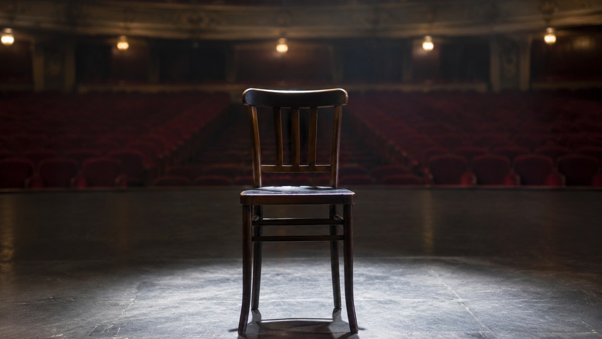 Una butaca vacía en un escenario teatral iluminado, en homenaje a la carrera de Patrick Stewart.